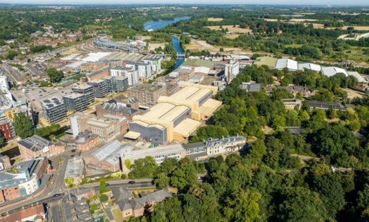 Aerial photo view of site showing residential tower blocks and large office buildings to the left with tree filled area to the right