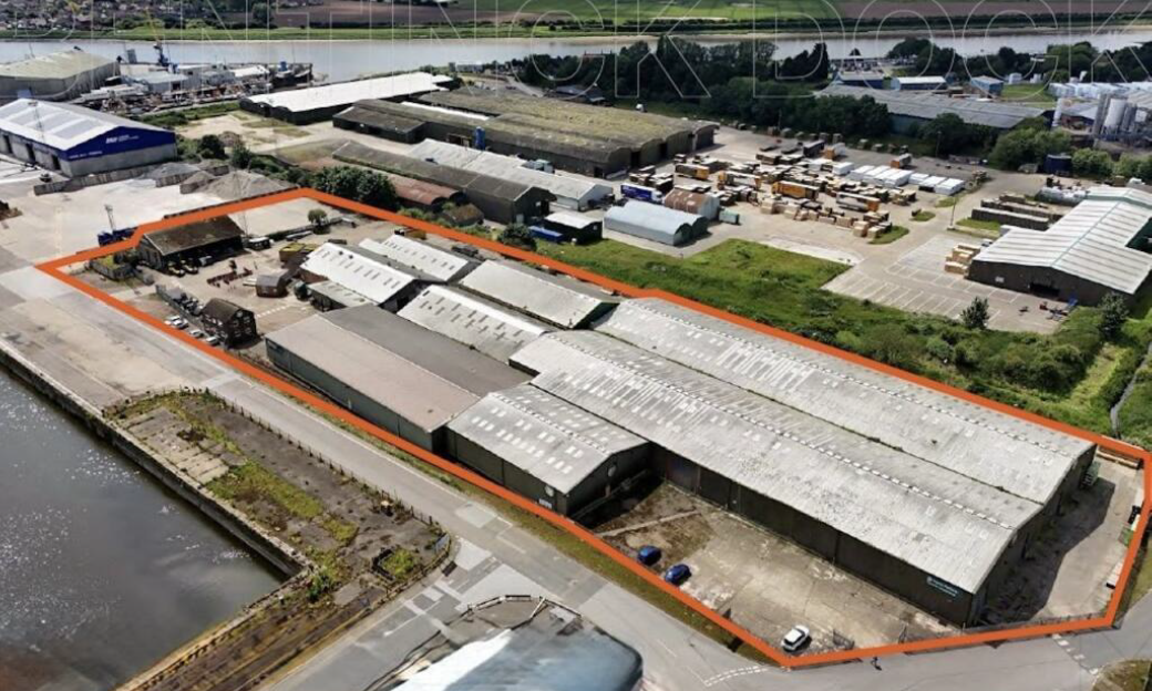 Oblique aerial photo of site including large industrial buildings, with perimeter of area outlined in red