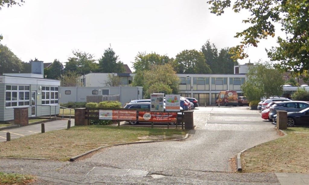 Oblique aerial photo of site including a large building surrounded by a carpark, with perimeter of area outlined in orange